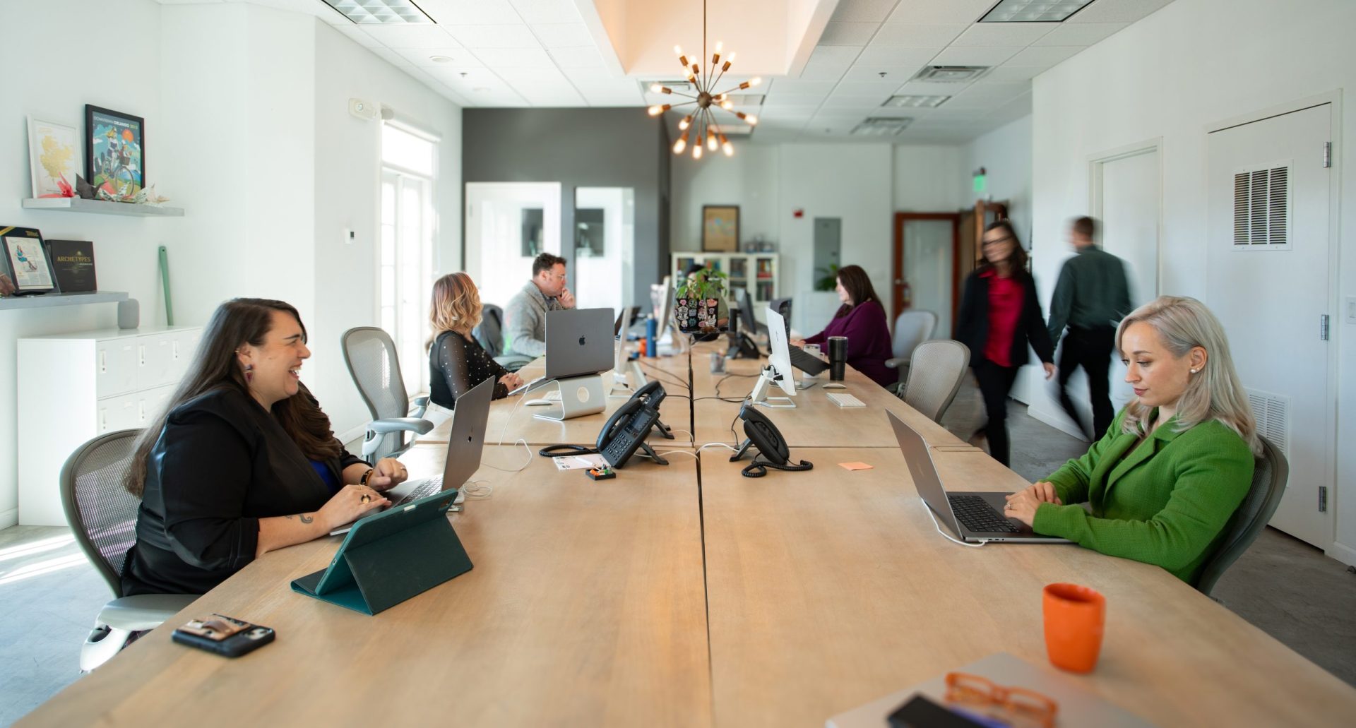 team members smiling sitting at open seating and walking past desks in a small studio office